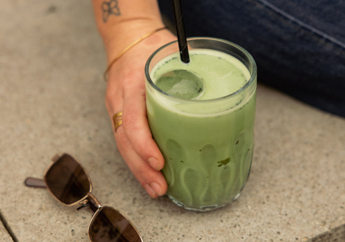 A Wholeday matcha pouch with a latte, a bamboo whisk in matcha powder, and an iced matcha in hand