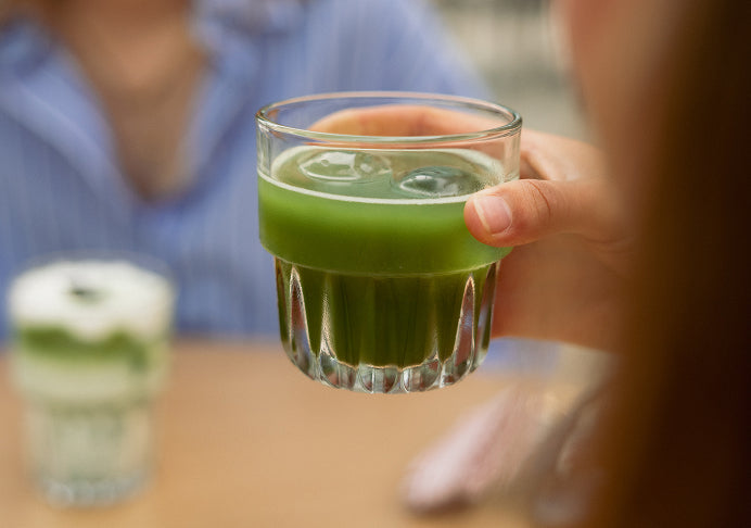 A Wholeday matcha pouch with a latte, a bamboo whisk in matcha powder, and an iced matcha in hand